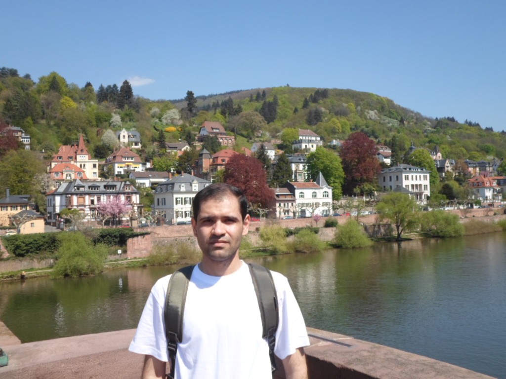 Dr. Mahdi Kohandani am Neckarufer in Heidelberg, im Hintergrund Häuser an einem bewaldeten Hang